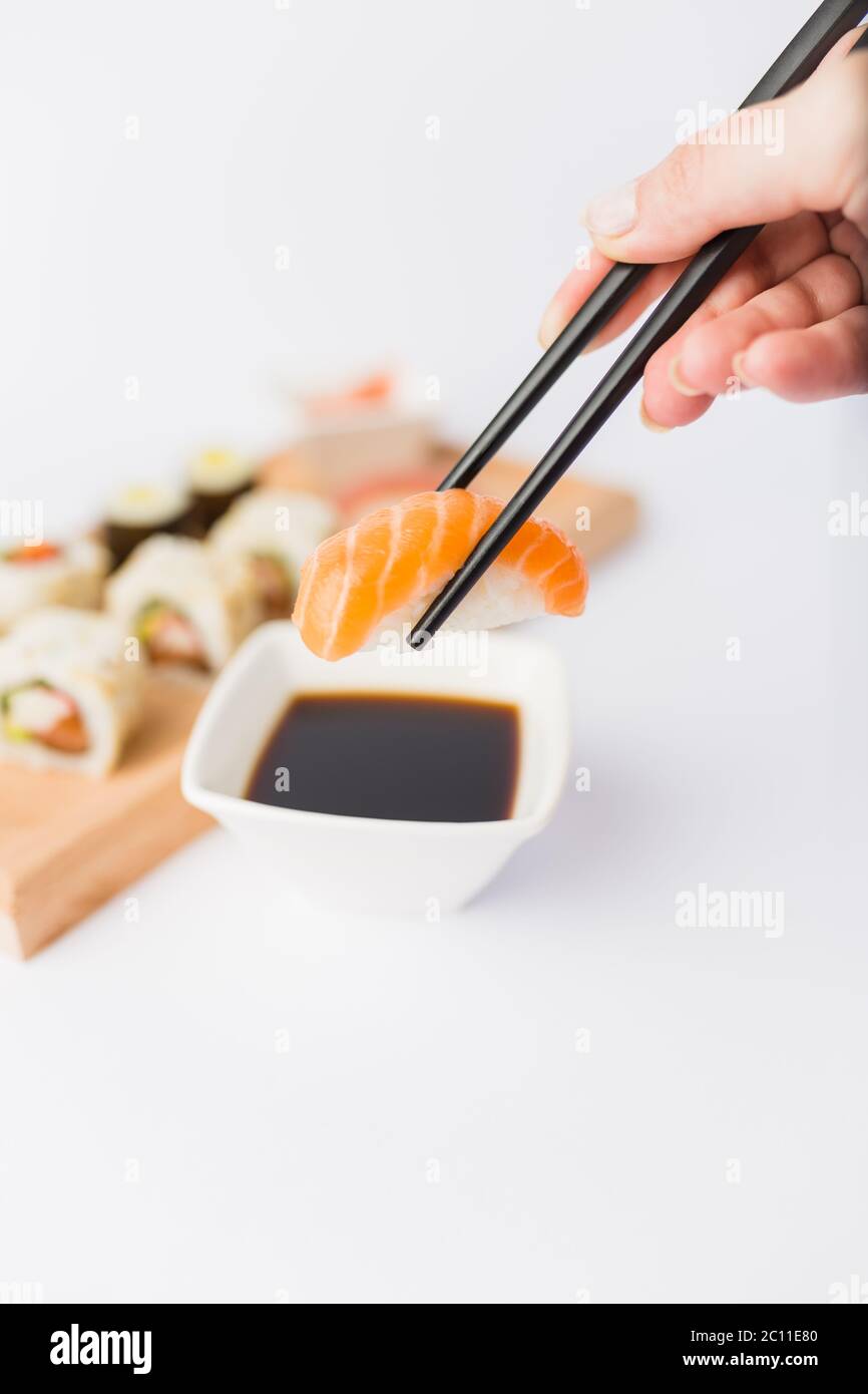 Gros plan de la femme tenant des baguettes avec un rouleau de sushi au saumon et un bol avec sauce soja sur la table, portion de repas japonais traditionnel en arrière-plan. Banque D'Images