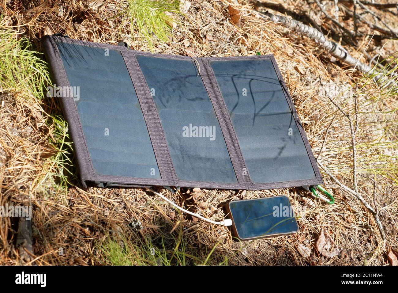 Le panneau solaire pliable se trouve sur la surface du sol forestier et charge le smartphone. Commodité pour les voyages et les longues promenades loin de traditio Banque D'Images