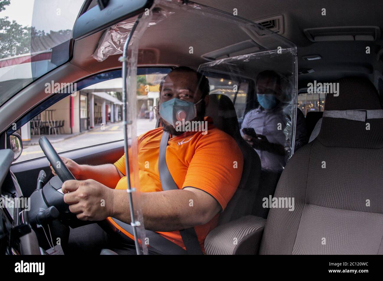 Ikhsan (37), un chauffeur de taxi en ligne portant un masque facial,  lorsqu'il conduit à l'aide d'une barrière en plastique au chauffeur dans la  rue de Bogor, en Indonésie, le 13 juin