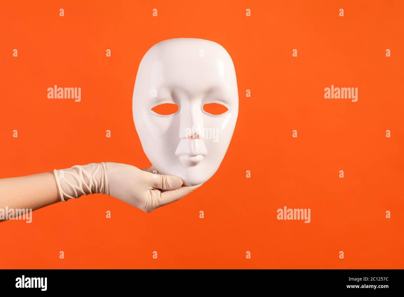 Vue latérale du profil gros plan de la main humaine en gants chirurgicaux blancs tenant le masque blanc. Prise de vue en studio, à l'intérieur, isolée sur fond orange. Banque D'Images
