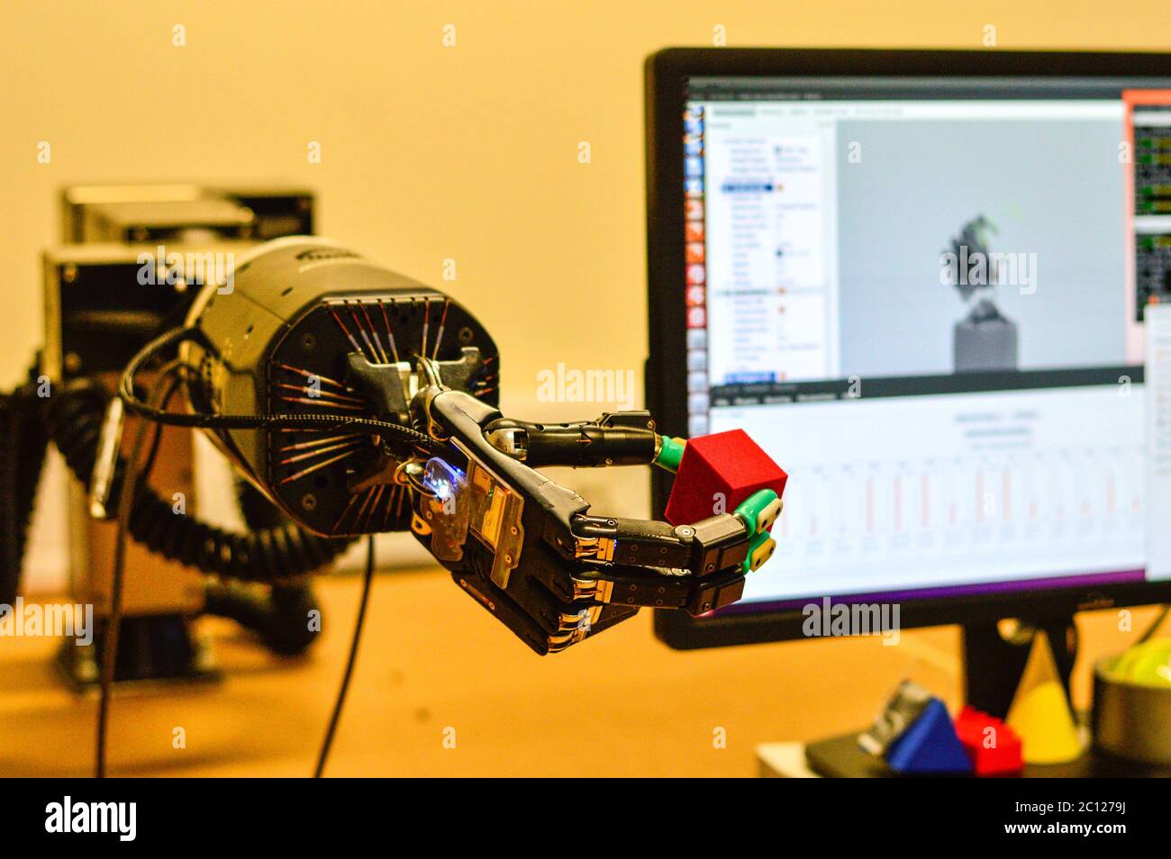 La main robot tient un cube rouge dans le laboratoire de recherche. Écran d'ordinateur flou en arrière-plan. Banque D'Images