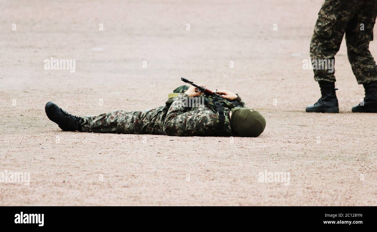 Homme dans militaire vêtements de camouflage et un masque allongé sur son dos le sable avec mitrailleuses en main pendant la démonstration Banque D'Images