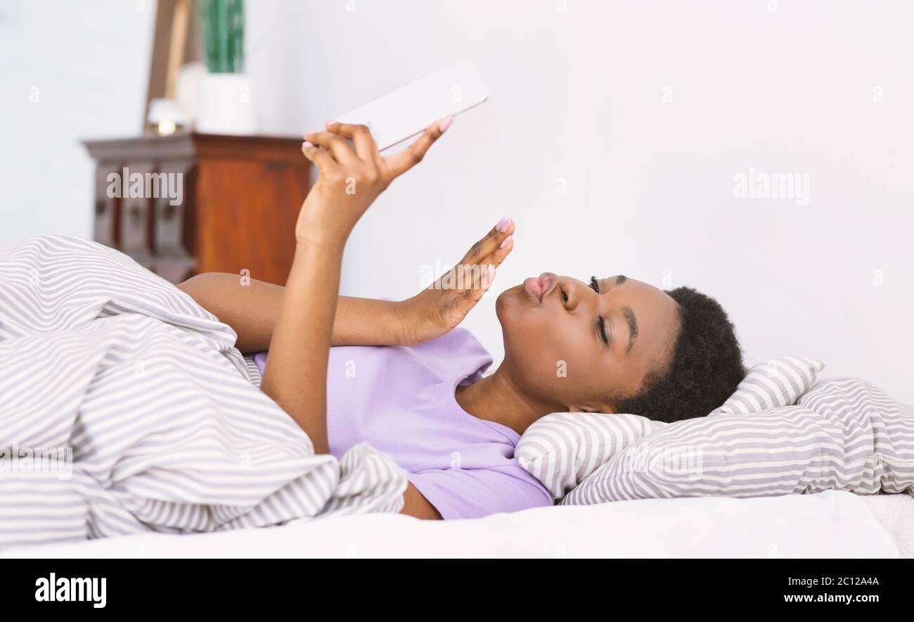 J'adore discuter. Une fille afro-américaine fait un baiser soufflant sur un smartphone et tient le téléphone à la main Banque D'Images