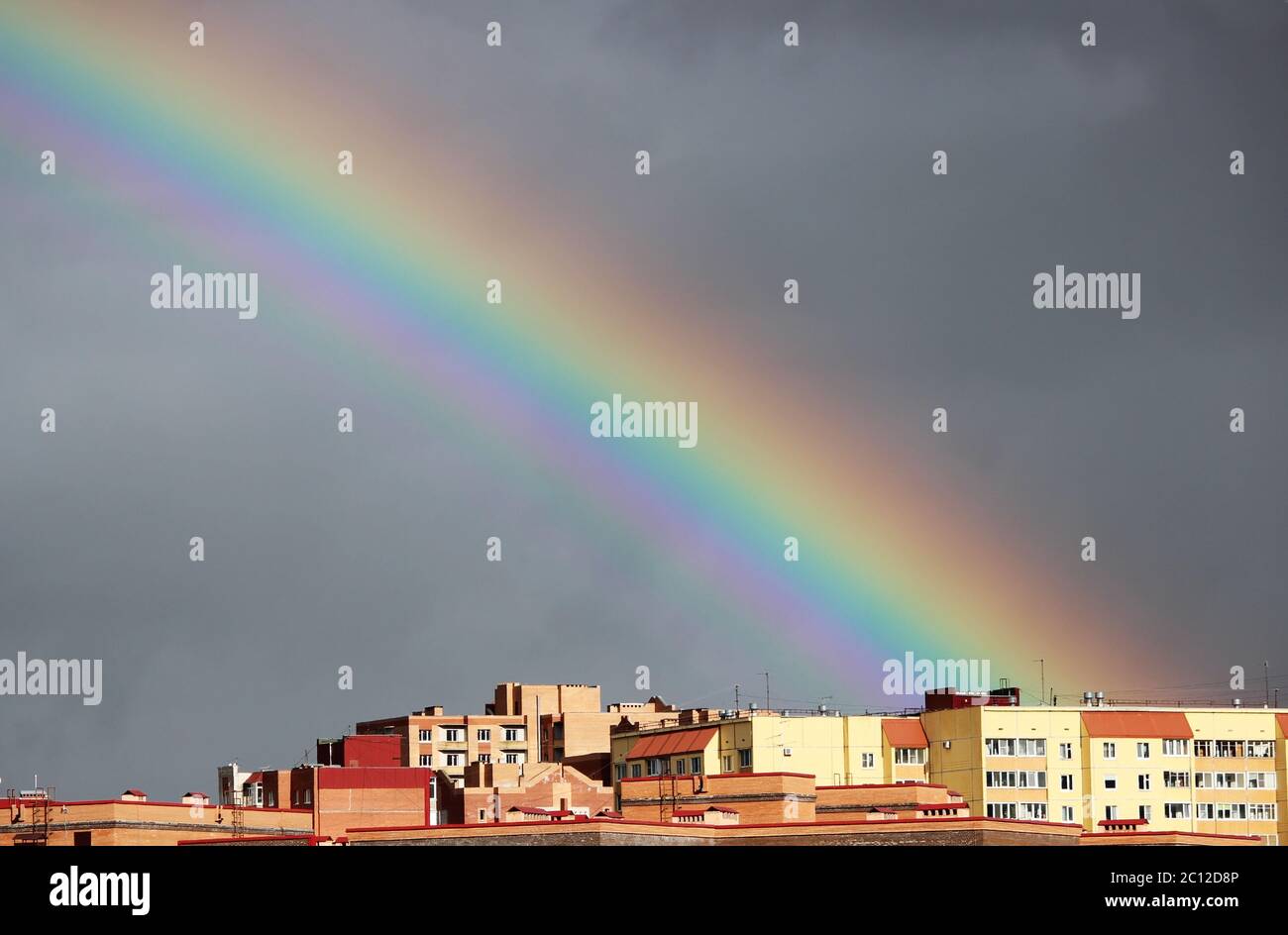 Arc-en-ciel coloré multicolore après la tempête dans le ciel gris au-dessus des maisons de ville Banque D'Images