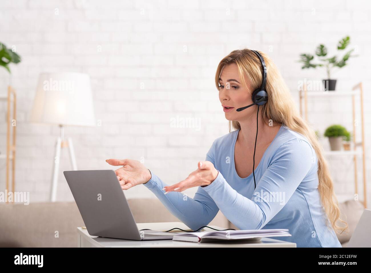 Réunion d'affaires en ligne. Une femme adulte avec casque communique avec le client sur un ordinateur portable Banque D'Images