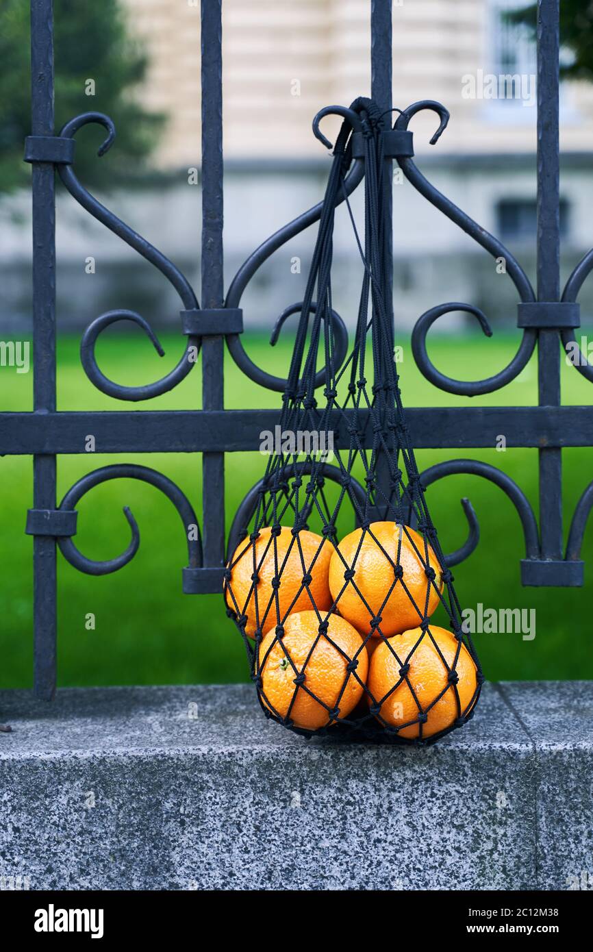 Sac en maille noire plein d'oranges comme symbole de style de vie zéro déchet est suspendu sur la clôture en fer forgé Banque D'Images