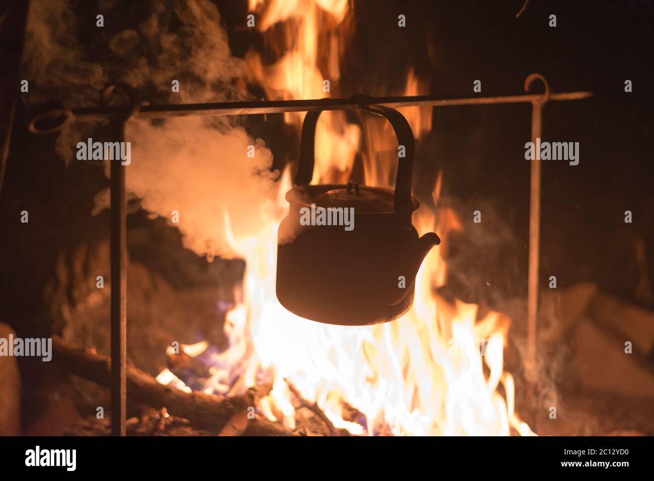 La bouilloire est chauffée sur un feu lumineux la nuit à l'extérieur Banque D'Images