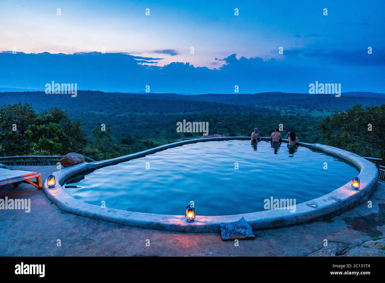 Trois personnes se détendent au crépuscule dans la piscine surplombant le parc national du lac Mburo à Mihingo Lodge, en Ouganda Banque D'Images