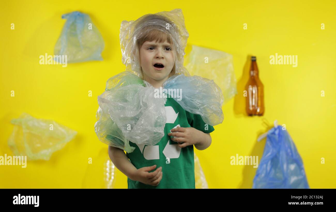 Triste activiste fille dans t-shirt avec le logo de recyclage dans des emballages en plastique sur son cou et la tête. Fond avec sacs de cellophane, flacons. Réduire la pollution par les déchets de plastique. Pensez vert. Sauver l'environnement écologique Banque D'Images