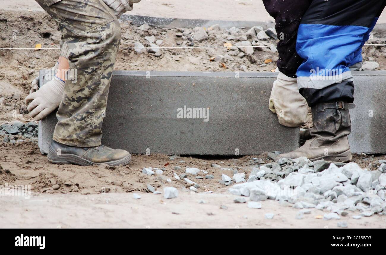 Les travailleurs soulèvent des bordures de béton. Installation d'une bordure de trottoir en béton au niveau des bordures de trottoir. Remplacement du trottoir Banque D'Images