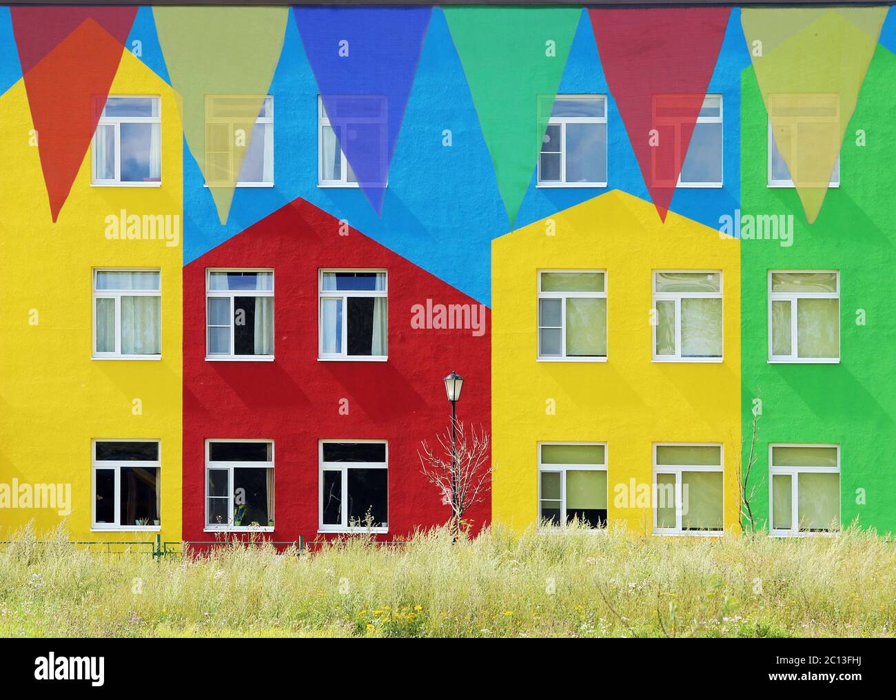 Drapeaux triangulaires multicolores suspendus dans le ciel à une piscine sur fond de maisons colorées. Banque D'Images