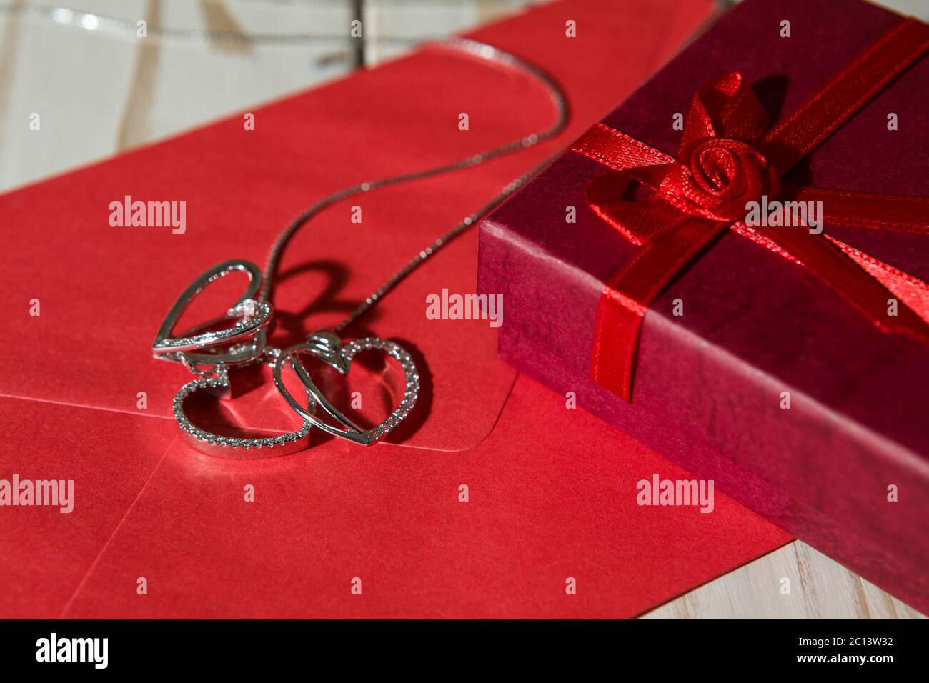 Gros plan des pendentifs coeur argenté sur une enveloppe rouge et une boîte cadeau Banque D'Images
