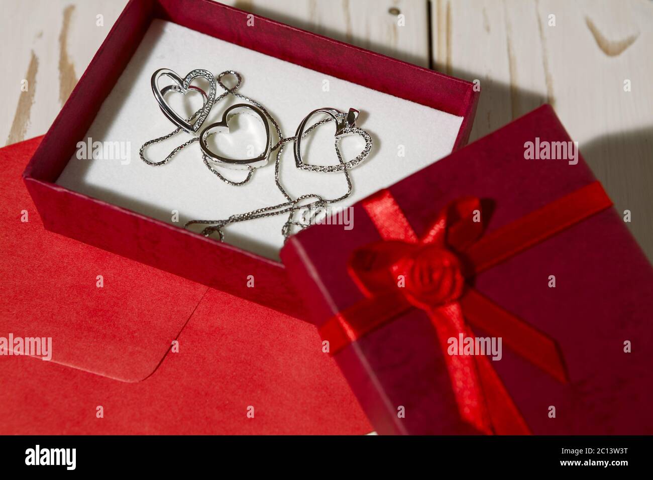 Gros plan des pendentifs coeur argenté dans une boîte cadeau rouge et une enveloppe rouge Banque D'Images