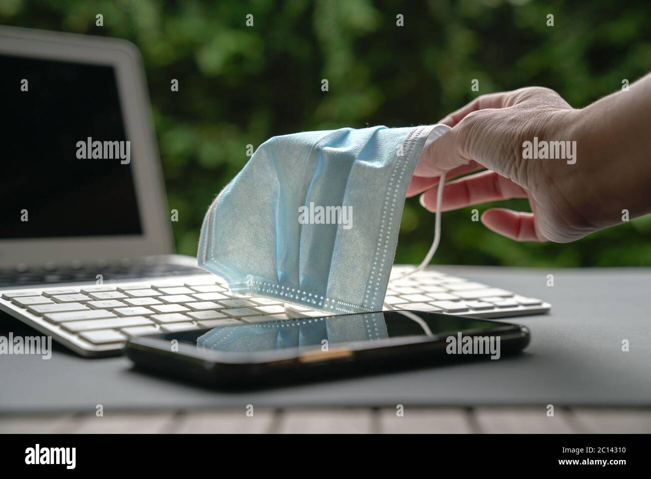 Femme tenant un masque médical avec un clavier d'ordinateur portable et un téléphone portable en vue. Travaillez à la maison pendant le concept Covid-19. Banque D'Images