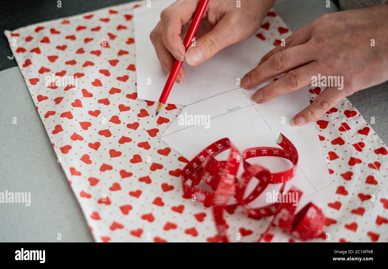 Une femme avec travaille avec une règle de couture, prépare des matériaux de fabrication de masque à la maison avec le motif de coeur pendant COVID-19. Fashion, atelier de Tailor. Banque D'Images