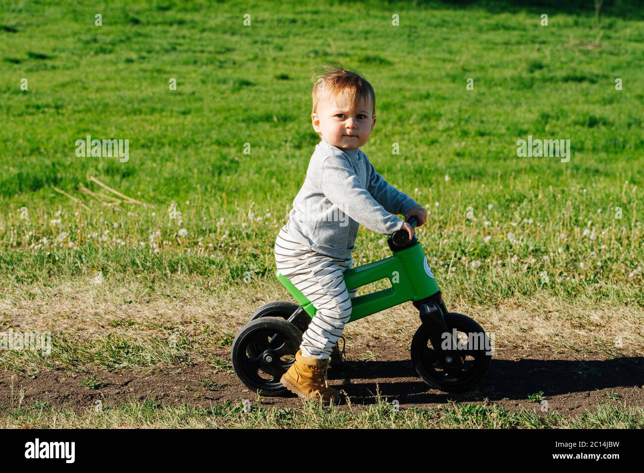 Un petit enfant grincheux sur un vélo à trois roues. Il regarde la caméra. Banque D'Images