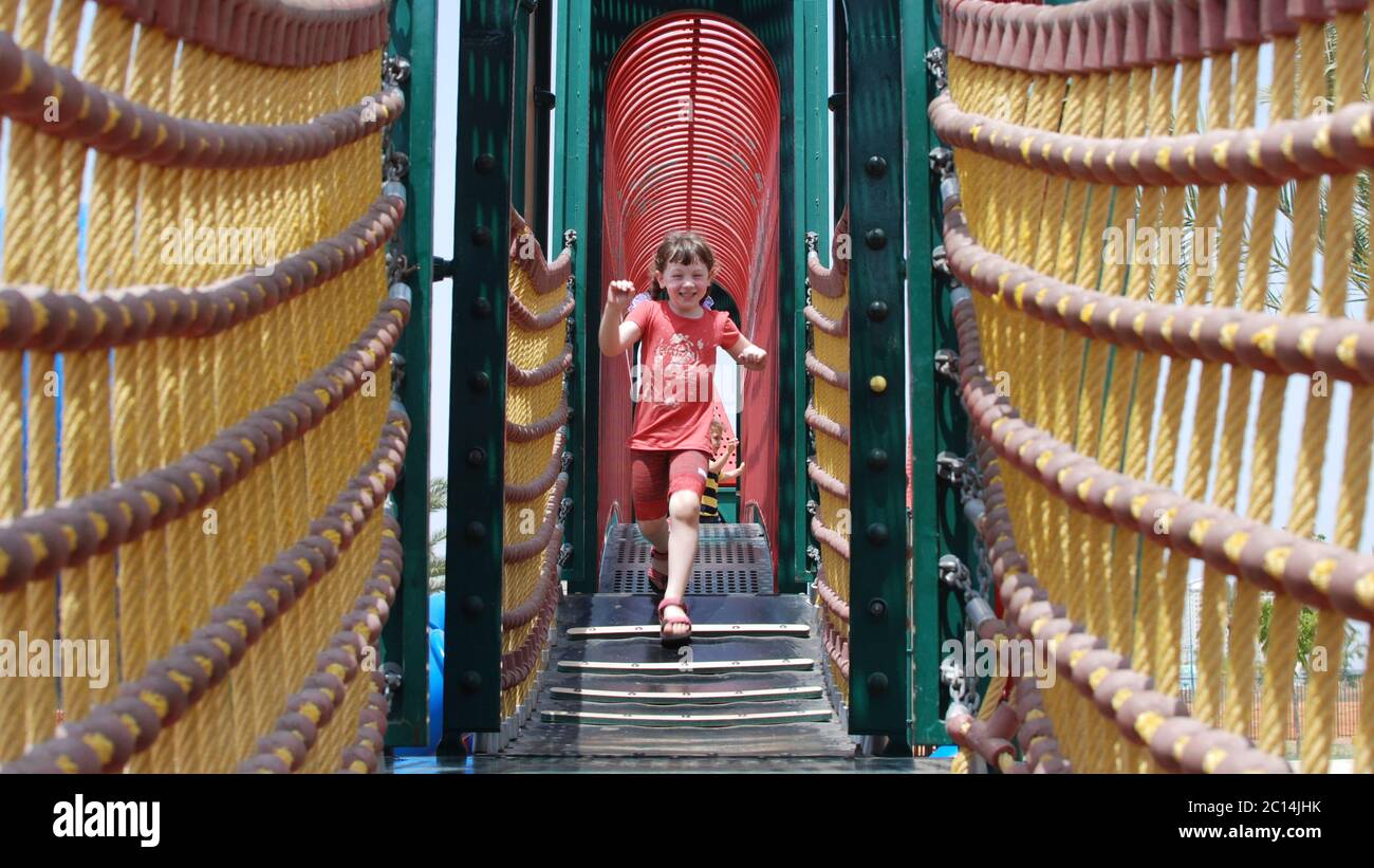 Une jeune fille excitée de 5 court sur un pont de corde dans un terrain de jeu modèle disponible Banque D'Images