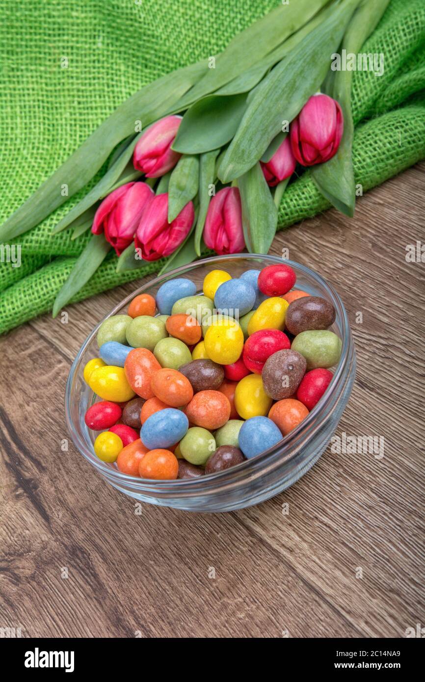 Bonbons colorés dans un bol en verre avec tulipes sur fond de bois Banque D'Images