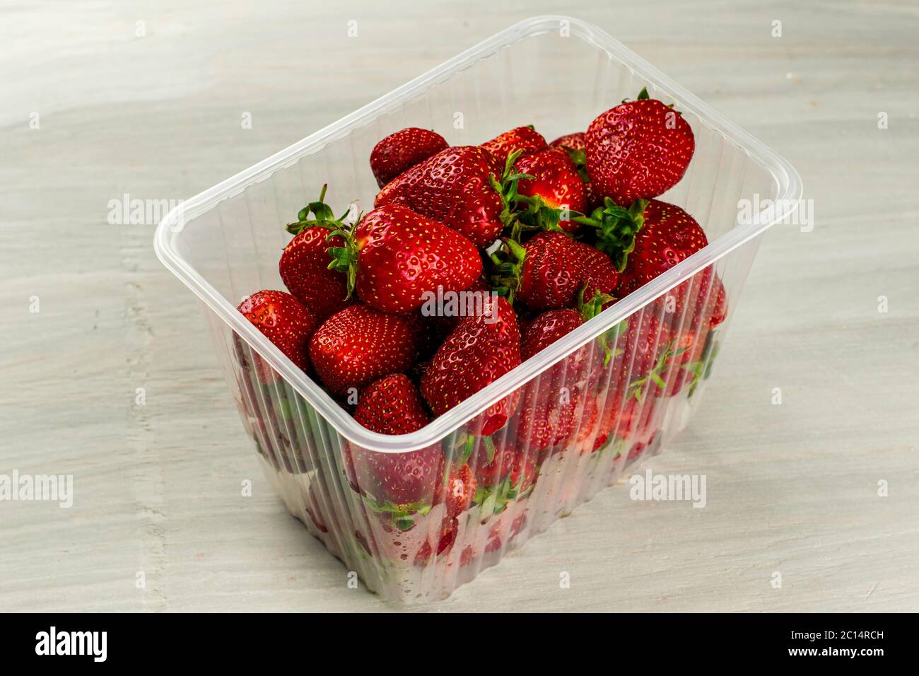 un récipient en plastique transparent avec des fraises rouges juteuses mûres est sur la table Banque D'Images