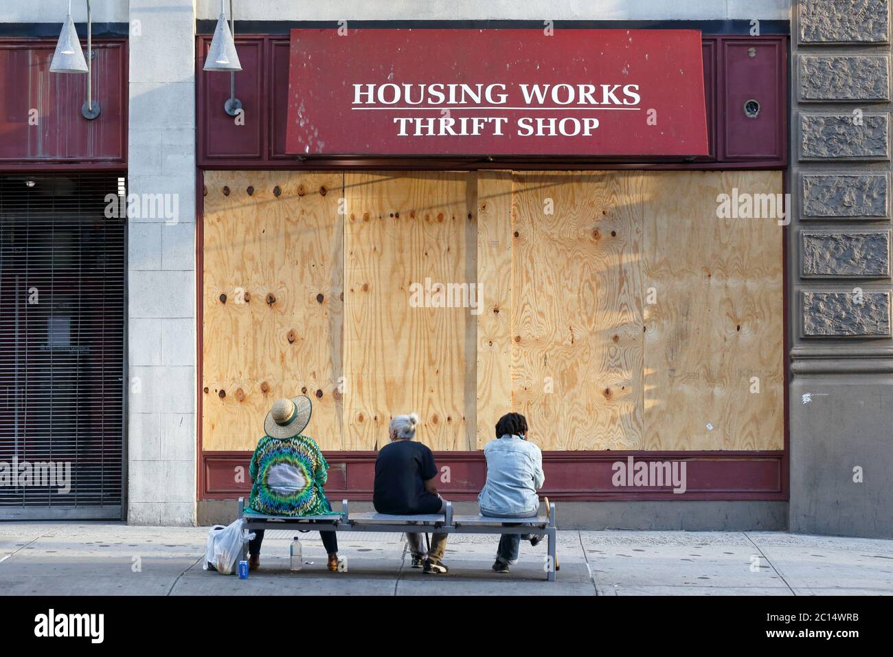 Personnes assises sur un banc devant un volet, monté à bord, fermé, Housing Works Thrift Shop à Manhattan, New York, NY. 6 juin 2020. Banque D'Images