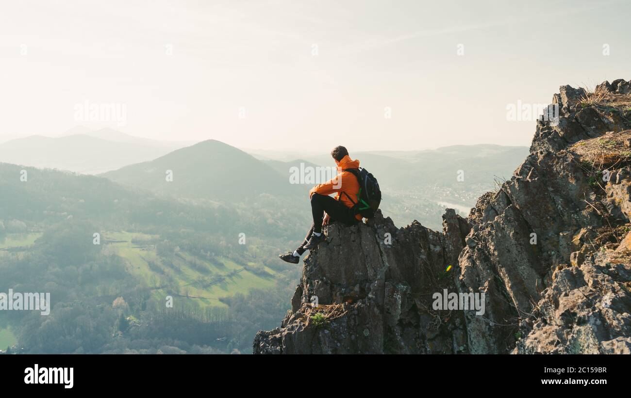 Jeune homme avec sac à dos assis sur le rocher regardant dans le paysage. Écouter le silence. Beau moment le miracle de la nature. Banque D'Images