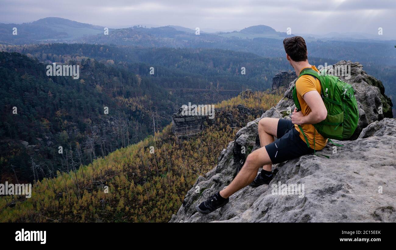 Un randonneur intrépide dans des vêtements de sport assis au bord de la falaise. Roche de grès, paysage vallonné de la forêt et vue sur le vert. Parc naturel seul avec la nature. Banque D'Images