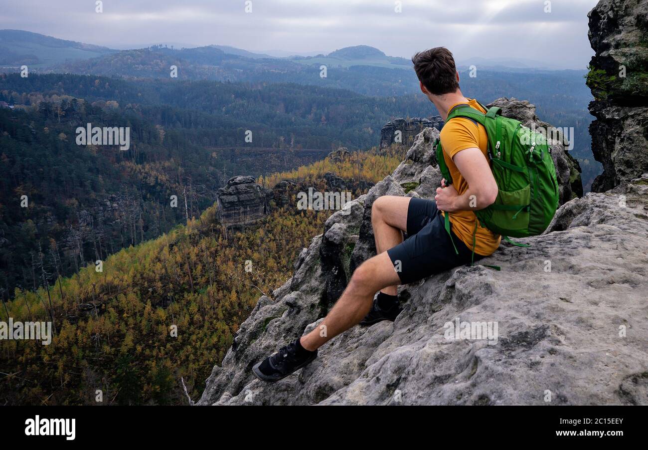 Un randonneur intrépide dans des vêtements de sport assis au bord de la falaise. Roche de grès, paysage vallonné de la forêt et vue sur le vert. Parc naturel seul avec la nature. Banque D'Images