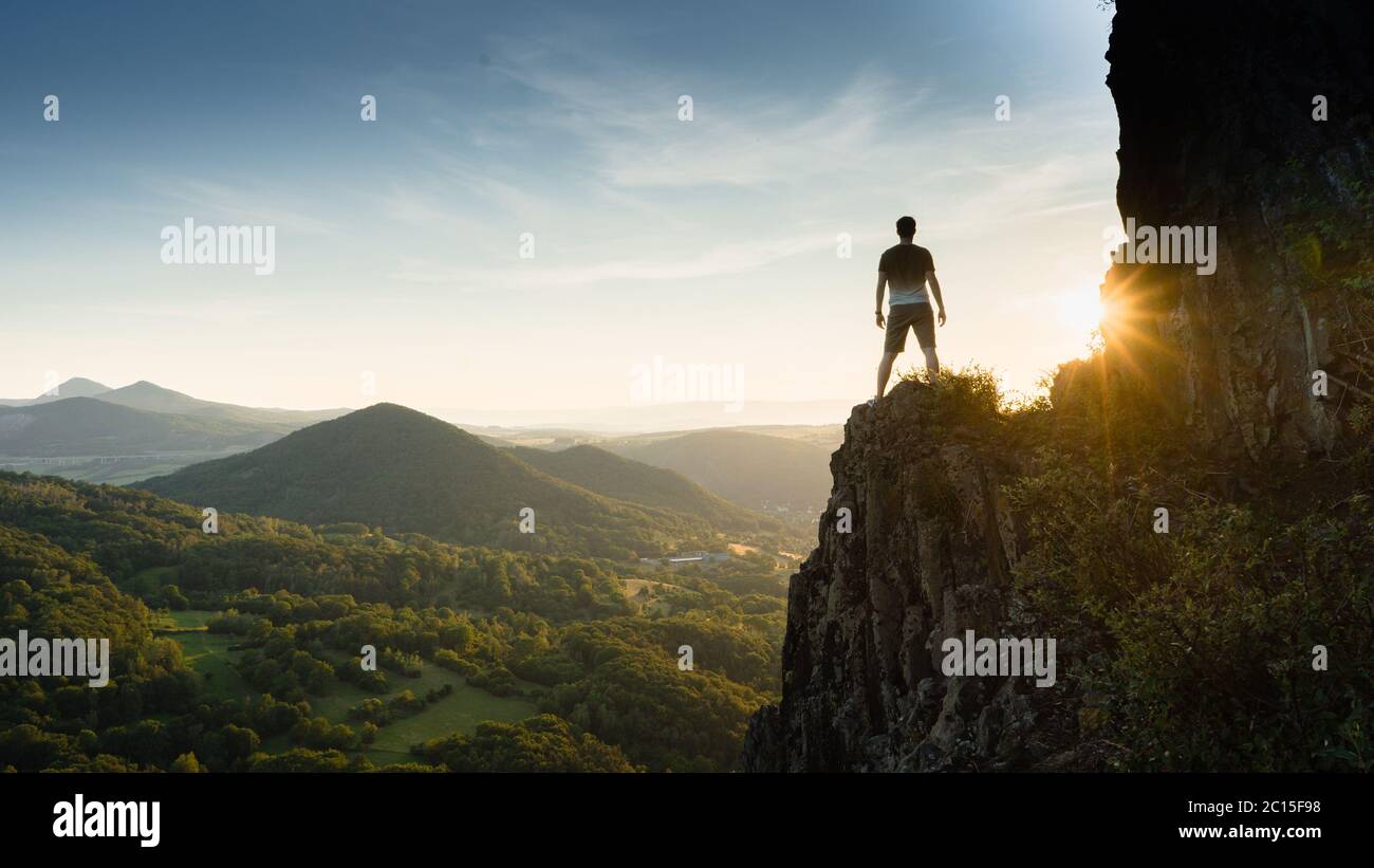 Silhouette de la personne sur le rocher au coucher du soleil. Satisfaire les randonneurs profiter de la vue. Homme haut sur une falaise rocheuse regardant vers le bas du paysage. Vif et puissant Banque D'Images