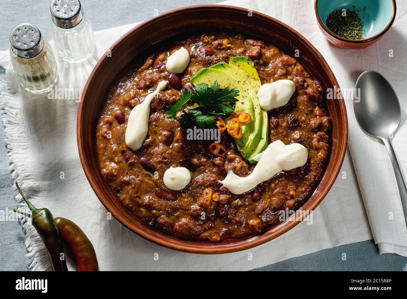 soupe de piment végétalien sans viande, avec haricots pinto et avocat, servie avec du yaourt à base de soja sur des nappes en lin Banque D'Images