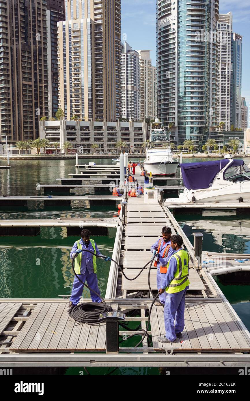 Dubaï / Émirats arabes Unis - 1 février 2020: Travailleurs immigrés à côté de yachts de luxe à Dubai Marina avec gratte-ciel en arrière-plan Banque D'Images