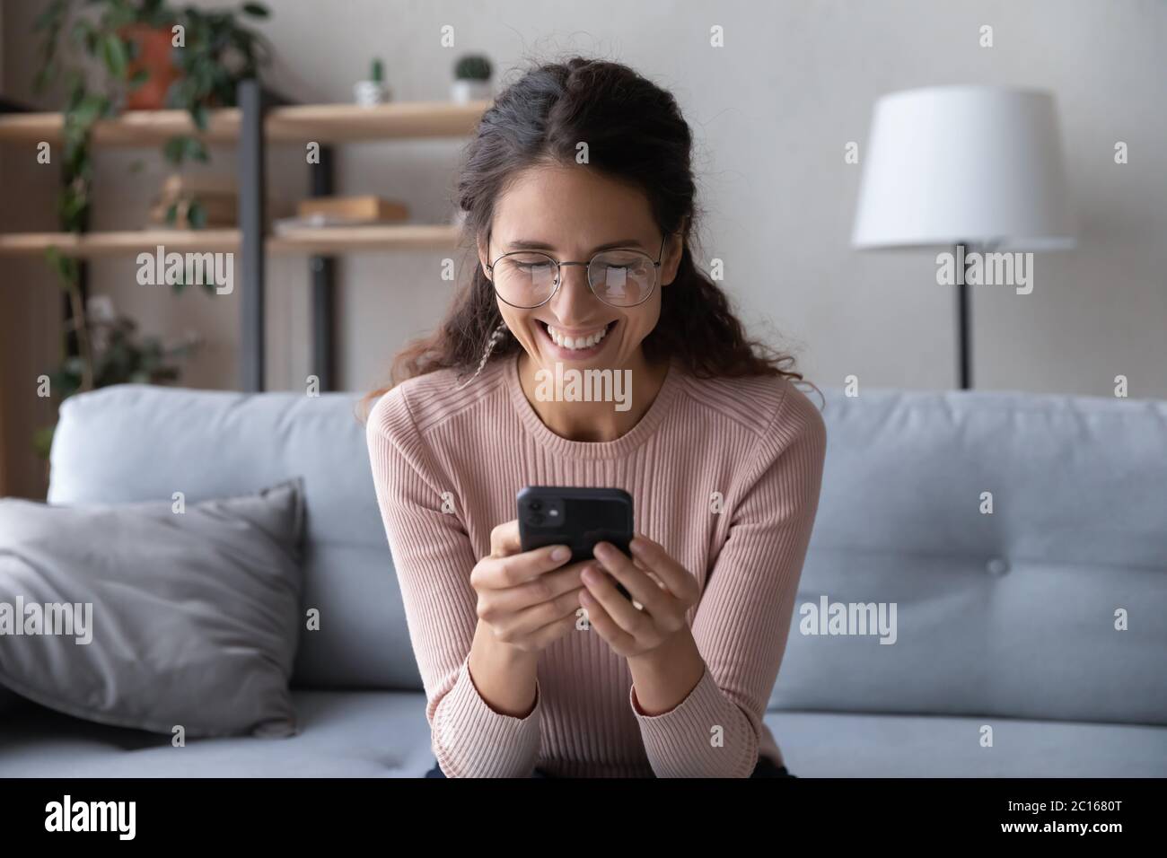 Femme souriante portant des lunettes regardant l'écran du smartphone, s'amusant Banque D'Images