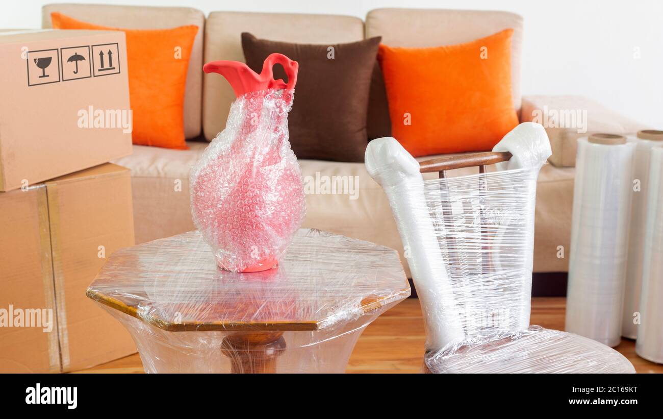 Scène en mouvement avec une approche à une chaise, un vase sur une table emballée en plastique à l'intérieur d'une pièce avec un canapé, des rouleaux en plastique et des boîtes en carton fermées sur W Banque D'Images