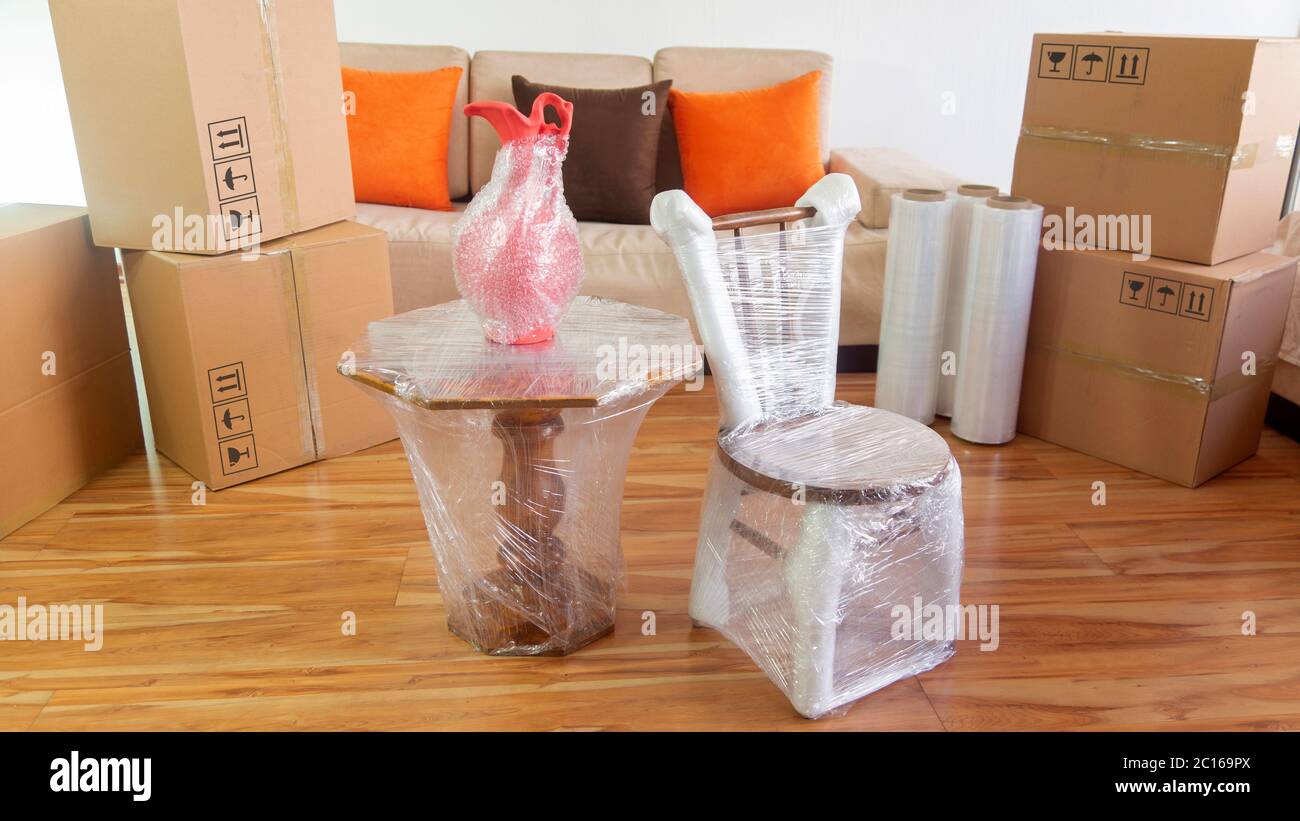 Scène en mouvement avec une chaise, un vase sur une table emballé en plastique à l'intérieur d'une pièce avec un canapé, des rouleaux en plastique et des boîtes en carton fermées sur fond blanc Banque D'Images