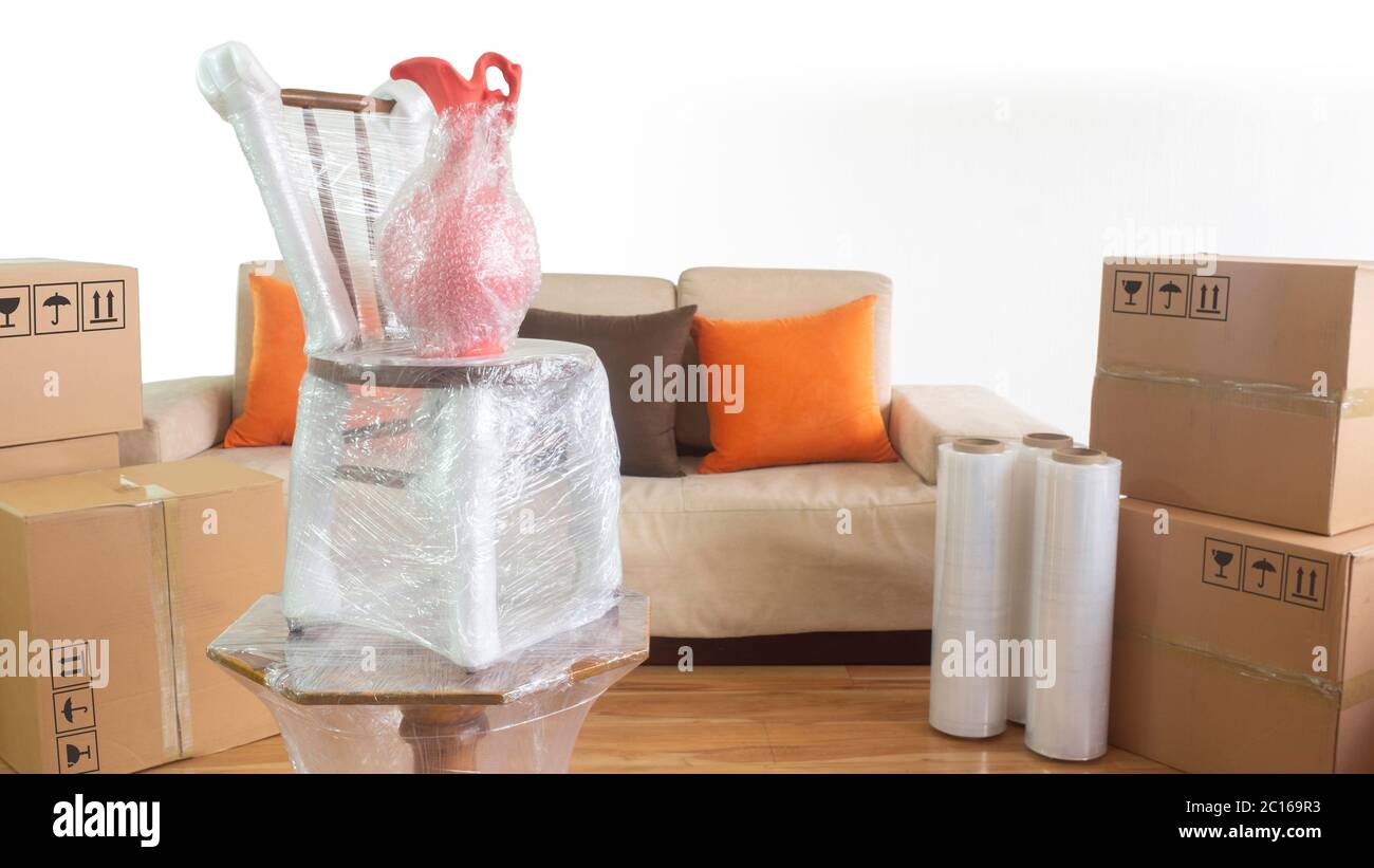 Scène en mouvement avec un vase sur une chaise sur une table emballée en plastique à l'intérieur d'une pièce avec un canapé, des rouleaux en plastique et des boîtes en carton fermées sur fond blanc Banque D'Images
