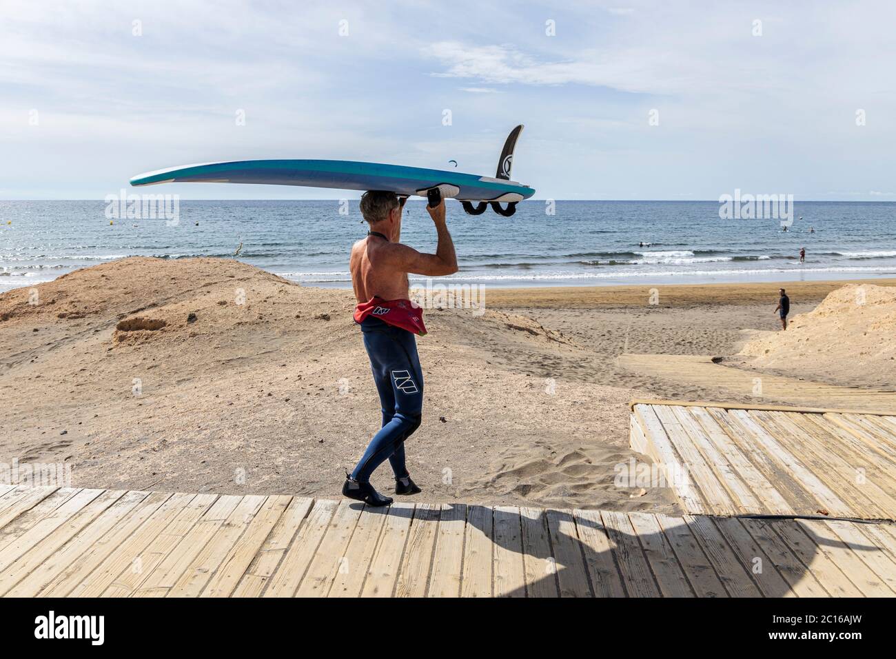 Les résidents locaux ont la plage pour eux-mêmes, car le temps monte pour l'été. Le surfeur porte sa planche sur la tête jusqu'au rivage. Phase 3 de-escalati Banque D'Images