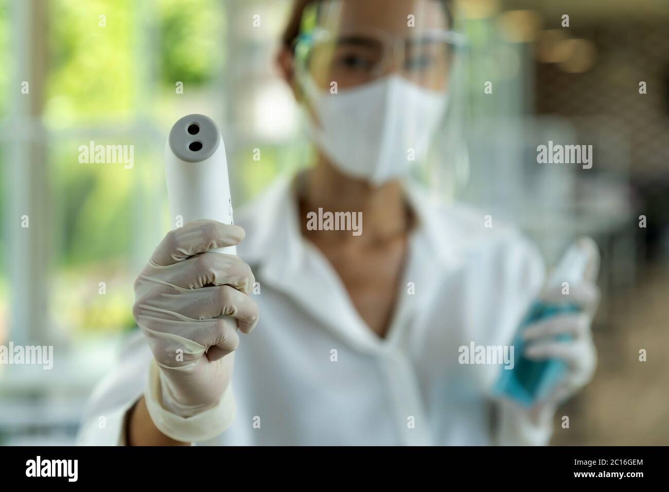 Portrait attrayant serveuse asiatique porter un masque et un masque facial tenir le thermomètre et l'assainisseur de gel d'alcool pour le nettoyage et l'hygiène avec le repos intérieur Banque D'Images