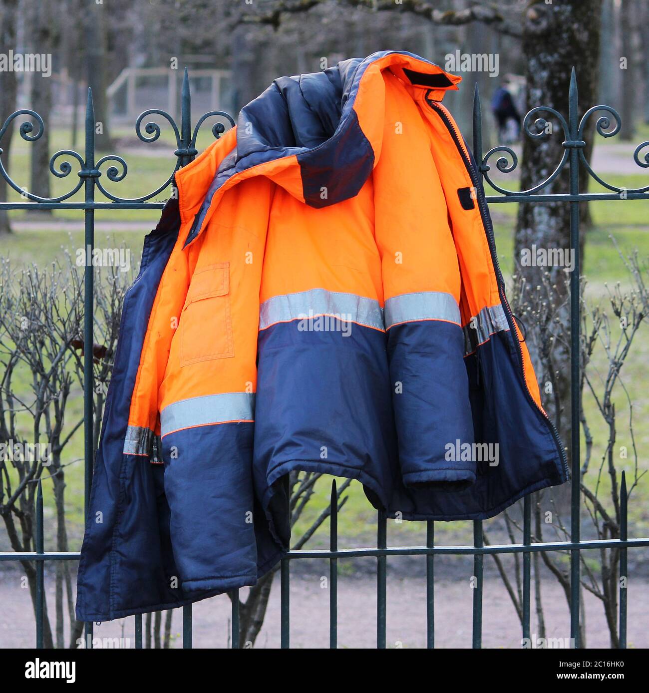 Veste chaude bleue-orange de travail suspendue sur la clôture. Banque D'Images