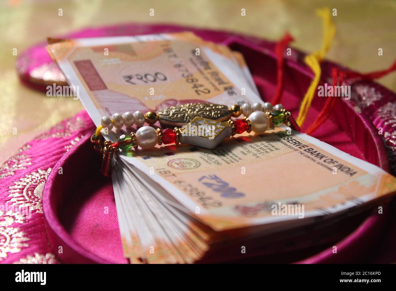 Raksha Bandhan concept de festival montrant le designer Rakhi ou Wrist Band Avec du riz et du kumkum épars, placés avec de la monnaie indienne sur coloré Banque D'Images Raksha Bandhan concept de festival montrant le designer Rakhi ou Wrist Band Avec du riz et du kumkum épars, placés avec de la monnaie indienne sur coloré Banque D'Images