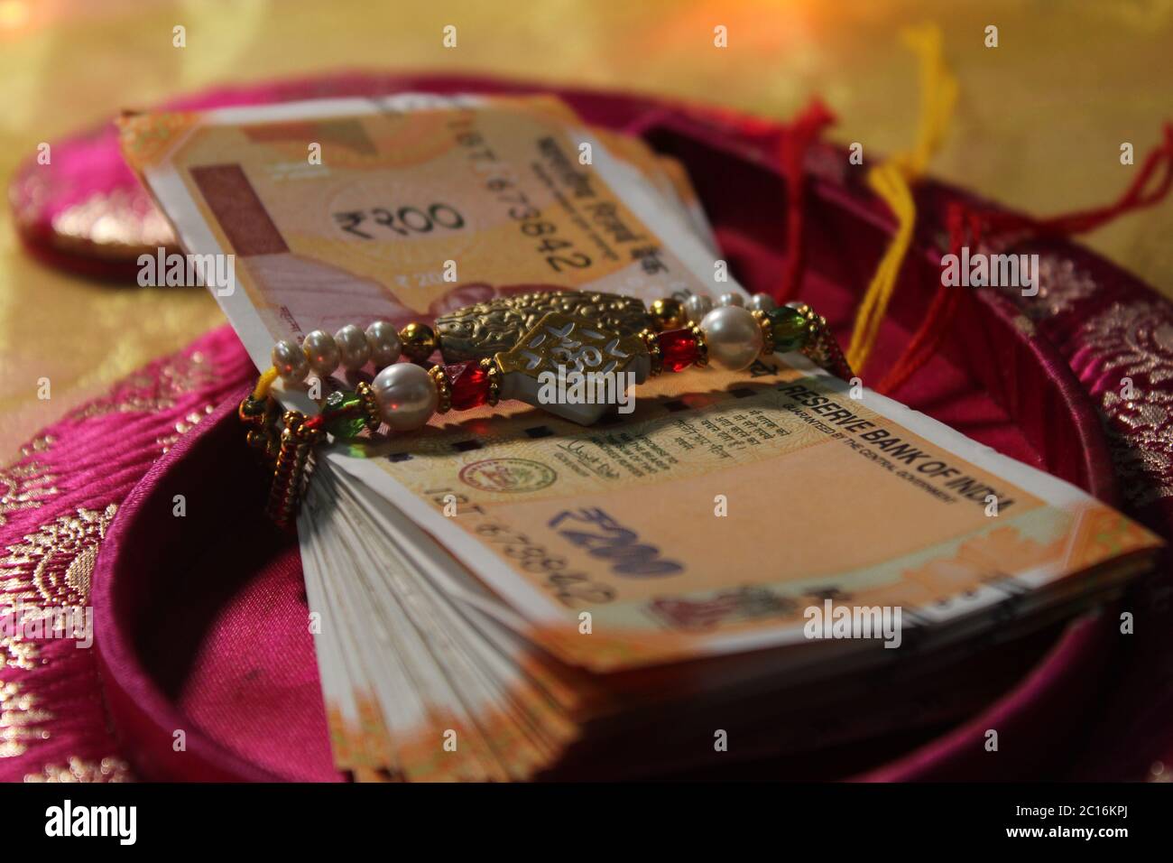 Raksha Bandhan concept de festival montrant le designer Rakhi ou Wrist Band Avec du riz et du kumkum épars, placés avec de la monnaie indienne sur coloré Banque D'Images Raksha Bandhan concept de festival montrant le designer Rakhi ou Wrist Band Avec du riz et du kumkum épars, placés avec de la monnaie indienne sur coloré Banque D'Images