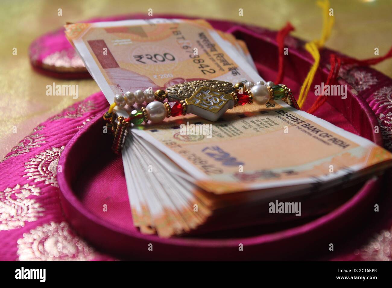 Raksha Bandhan concept de festival montrant le designer Rakhi ou Wrist Band Avec du riz et du kumkum épars, placés avec de la monnaie indienne sur coloré Banque D'Images Raksha Bandhan concept de festival montrant le designer Rakhi ou Wrist Band Avec du riz et du kumkum épars, placés avec de la monnaie indienne sur coloré Banque D'Images