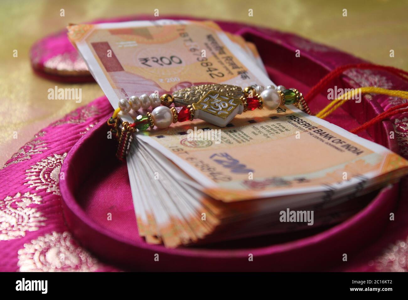Raksha Bandhan concept de festival montrant le designer Rakhi ou Wrist Band Avec du riz et du kumkum épars, placés avec de la monnaie indienne sur coloré Banque D'Images Raksha Bandhan concept de festival montrant le designer Rakhi ou Wrist Band Avec du riz et du kumkum épars, placés avec de la monnaie indienne sur coloré Banque D'Images
