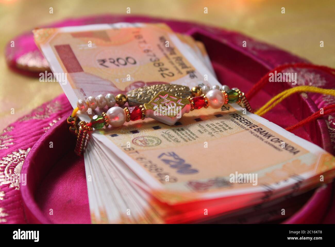 Raksha Bandhan concept de festival montrant le designer Rakhi ou Wrist Band Avec du riz et du kumkum épars, placés avec de la monnaie indienne sur coloré Banque D'Images Raksha Bandhan concept de festival montrant le designer Rakhi ou Wrist Band Avec du riz et du kumkum épars, placés avec de la monnaie indienne sur coloré Banque D'Images