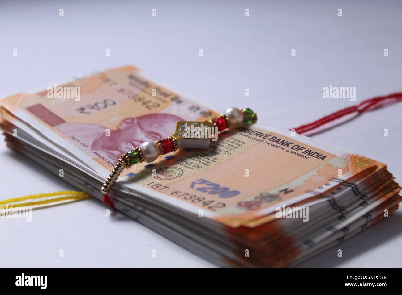 Raksha Bandhan concept de festival montrant le designer Rakhi ou Wrist Band Avec du riz et du kumkum épars, placés avec de la monnaie indienne sur coloré Banque D'Images Raksha Bandhan concept de festival montrant le designer Rakhi ou Wrist Band Avec du riz et du kumkum épars, placés avec de la monnaie indienne sur coloré Banque D'Images