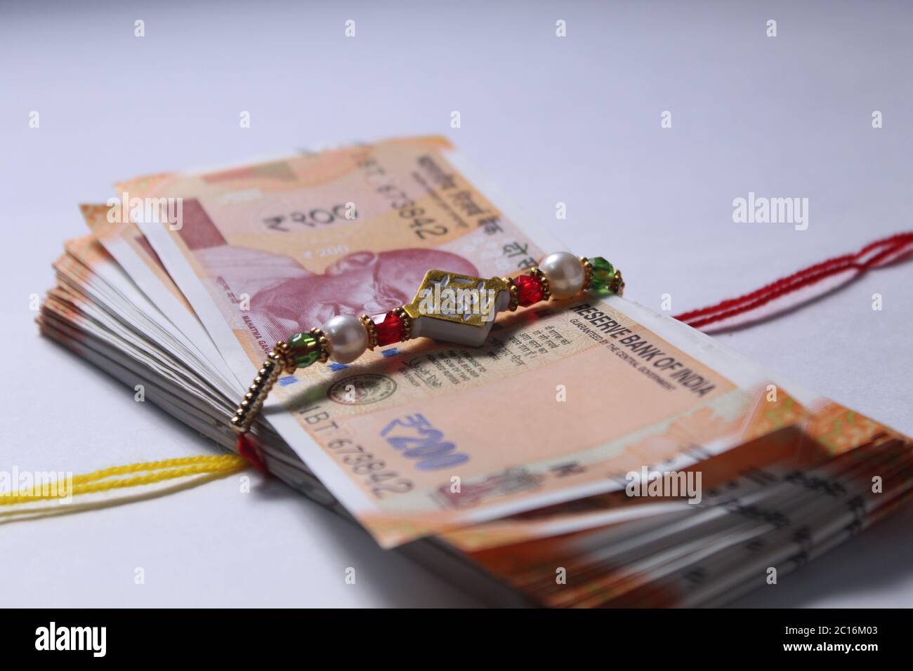 Raksha Bandhan concept de festival montrant le designer Rakhi ou Wrist Band Avec du riz et du kumkum épars, placés avec de la monnaie indienne sur coloré Banque D'Images Raksha Bandhan concept de festival montrant le designer Rakhi ou Wrist Band Avec du riz et du kumkum épars, placés avec de la monnaie indienne sur coloré Banque D'Images