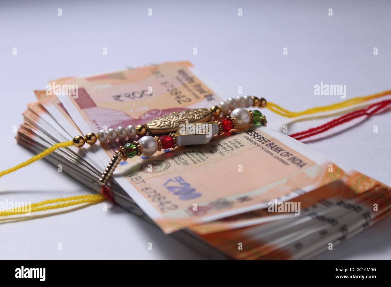 Raksha Bandhan concept de festival montrant le designer Rakhi ou Wrist Band Avec du riz et du kumkum épars, placés avec de la monnaie indienne sur coloré Banque D'Images Raksha Bandhan concept de festival montrant le designer Rakhi ou Wrist Band Avec du riz et du kumkum épars, placés avec de la monnaie indienne sur coloré Banque D'Images