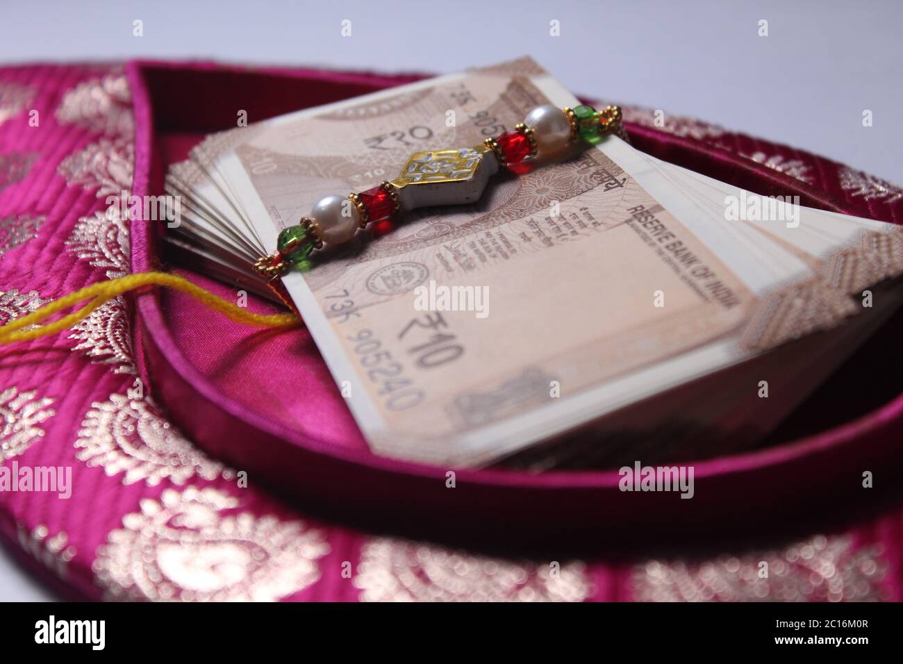 Raksha Bandhan concept de festival montrant le designer Rakhi ou Wrist Band Avec du riz et du kumkum épars, placés avec de la monnaie indienne sur coloré Banque D'Images Raksha Bandhan concept de festival montrant le designer Rakhi ou Wrist Band Avec du riz et du kumkum épars, placés avec de la monnaie indienne sur coloré Banque D'Images