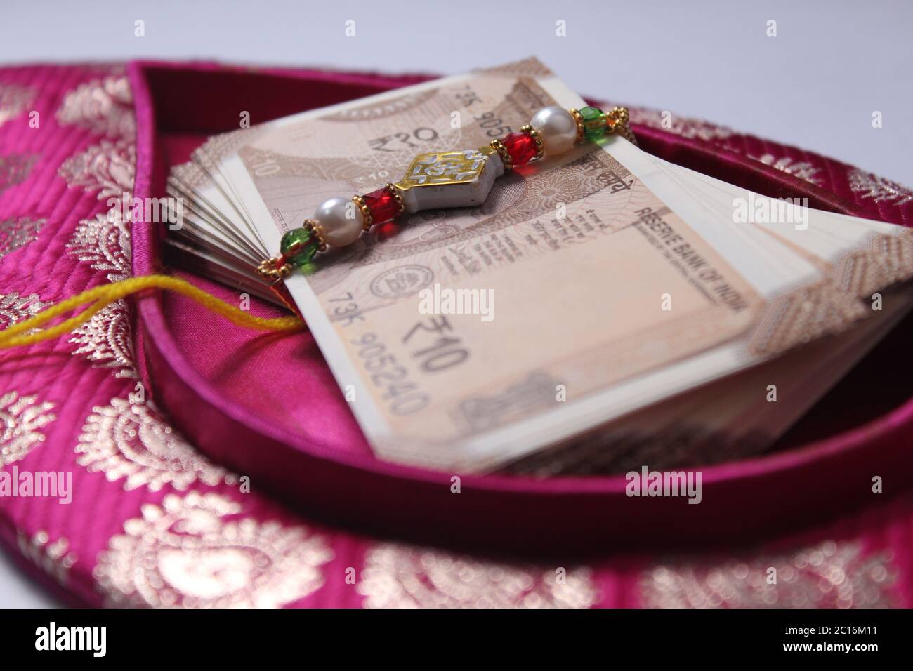 Raksha Bandhan concept de festival montrant le designer Rakhi ou Wrist Band Avec du riz et du kumkum épars, placés avec de la monnaie indienne sur coloré Banque D'Images Raksha Bandhan concept de festival montrant le designer Rakhi ou Wrist Band Avec du riz et du kumkum épars, placés avec de la monnaie indienne sur coloré Banque D'Images