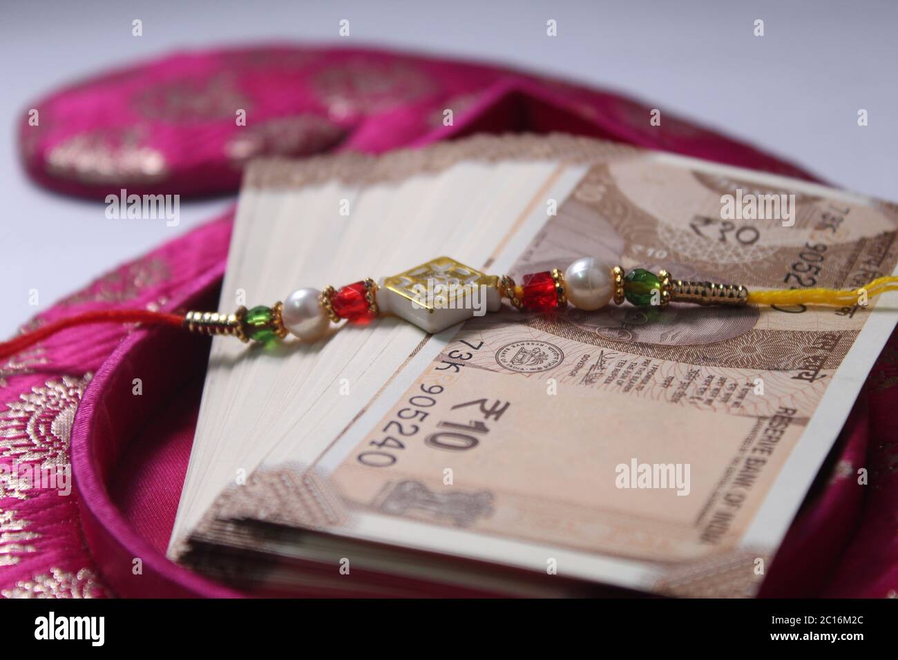 Raksha Bandhan concept de festival montrant le designer Rakhi ou Wrist Band Avec du riz et du kumkum épars, placés avec de la monnaie indienne sur coloré Banque D'Images Raksha Bandhan concept de festival montrant le designer Rakhi ou Wrist Band Avec du riz et du kumkum épars, placés avec de la monnaie indienne sur coloré Banque D'Images