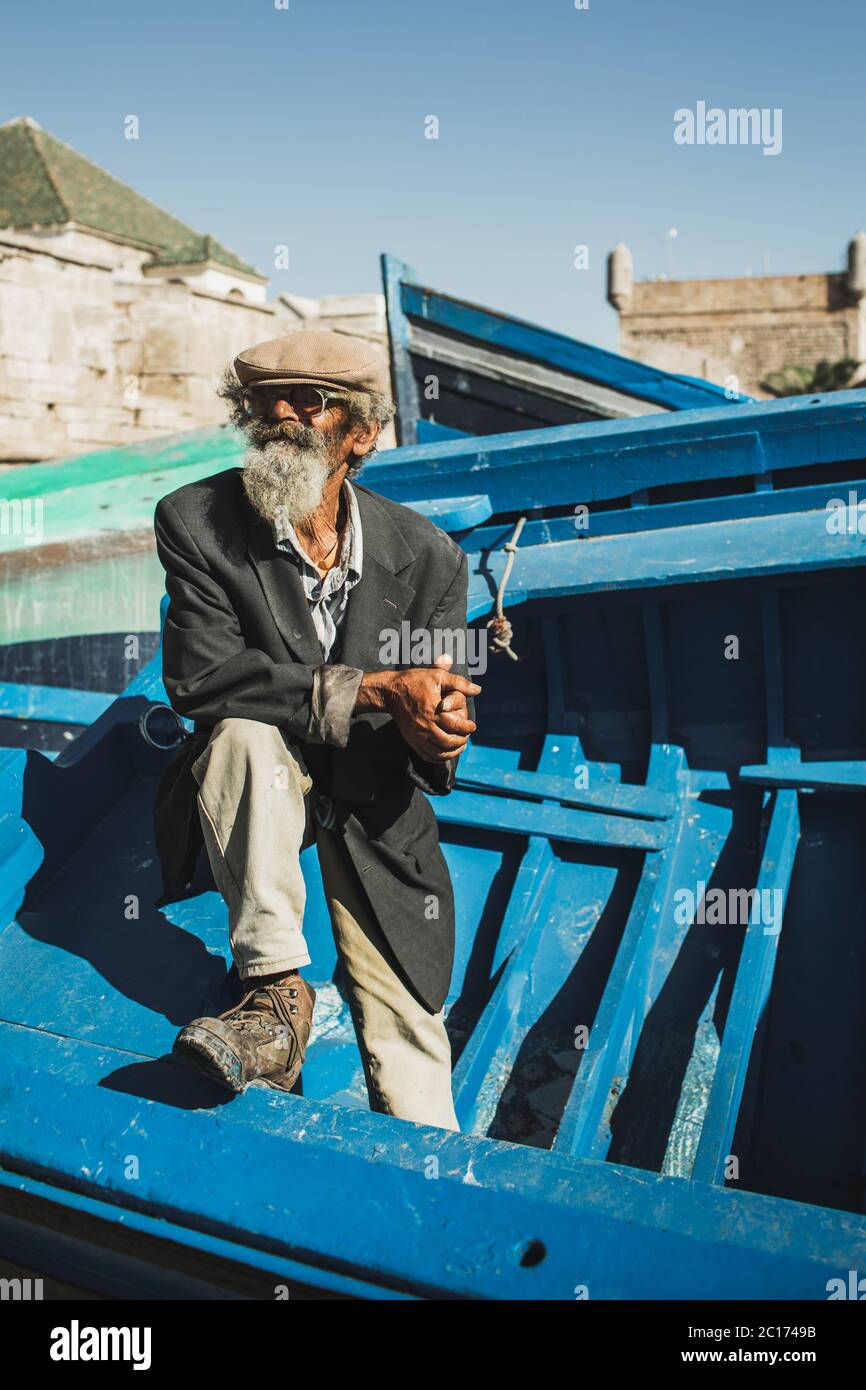 ESSAOUIRA, MAROC - 10 SEPTEMBRE 2019 : ancien pêcheur senior sur bateau en  bois bleu dans le port d'Essaouira. Look élégant, chapeau, barbe, lunettes  de soleil et veste. Le peuple marocain Photo Stock - Alamy