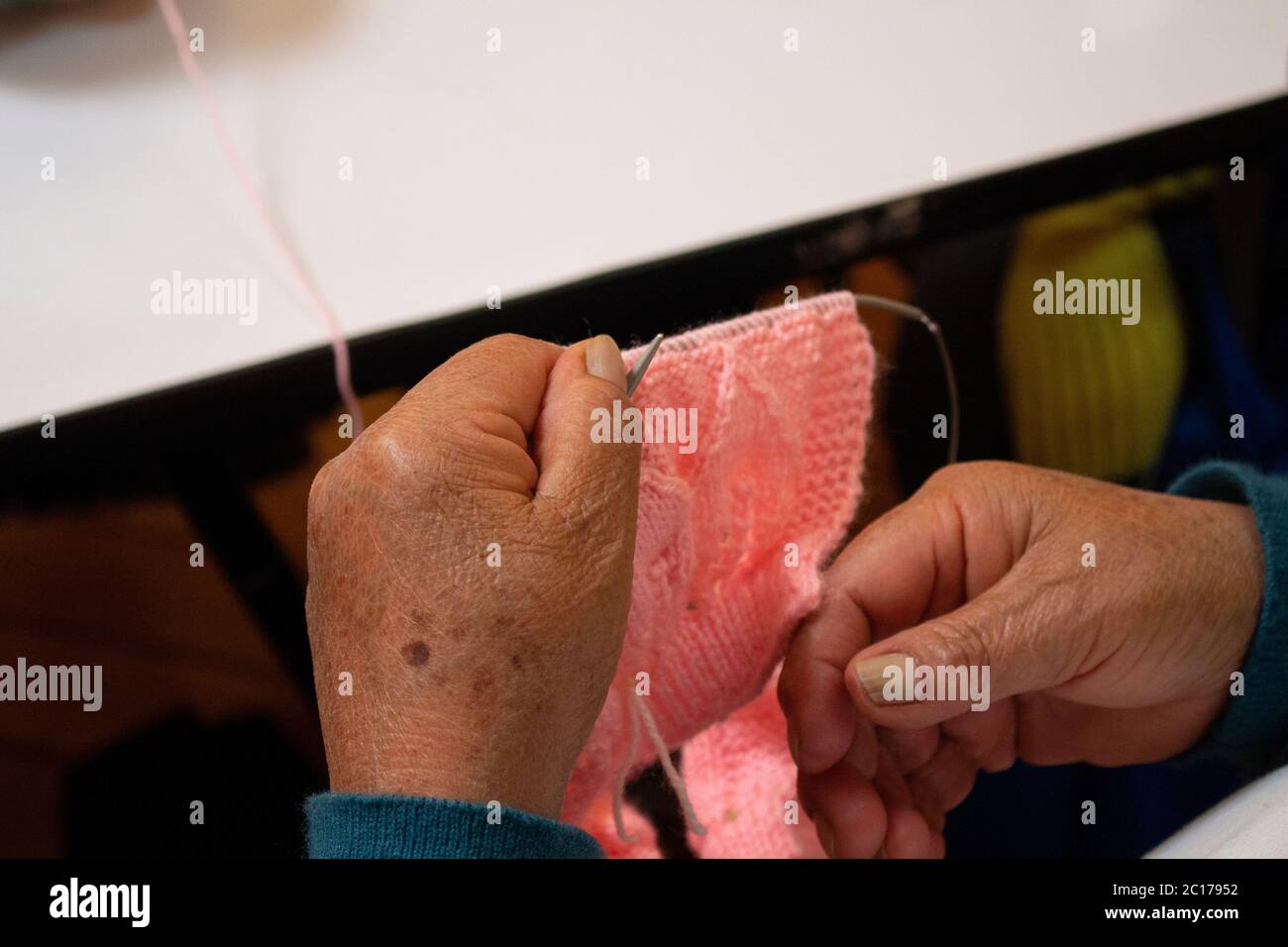 Gros plan des mains d'une vieille femme avec des aiguilles tricotées tricotage d'un vêtement en laine rose Banque D'Images